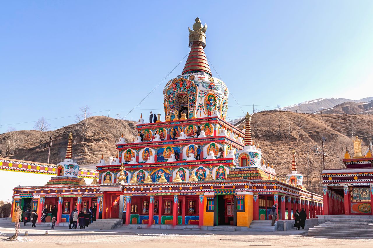 Colorful Tibetan stupa under clear blue sky at Serxu Monastery in China, showcasing traditional architecture.
